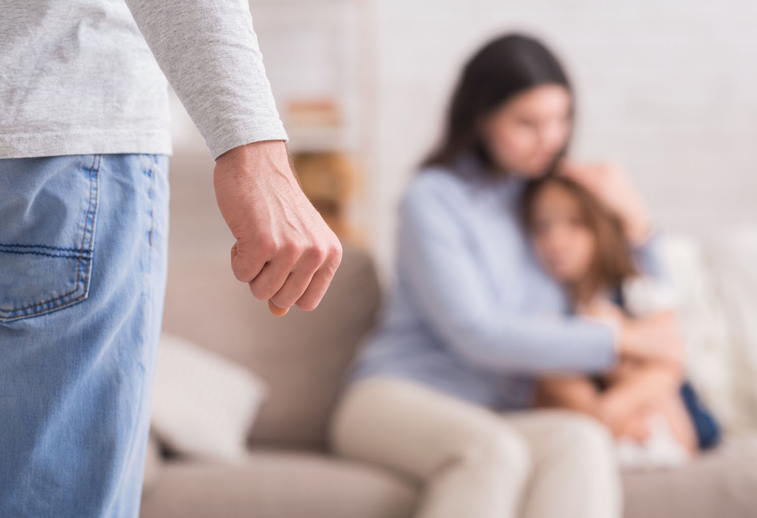 Mother holding her daughter as a man stands nearby with a clenched fist