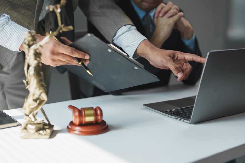 Lawyers reviewing a case on a laptop beside a Lady Justice statue